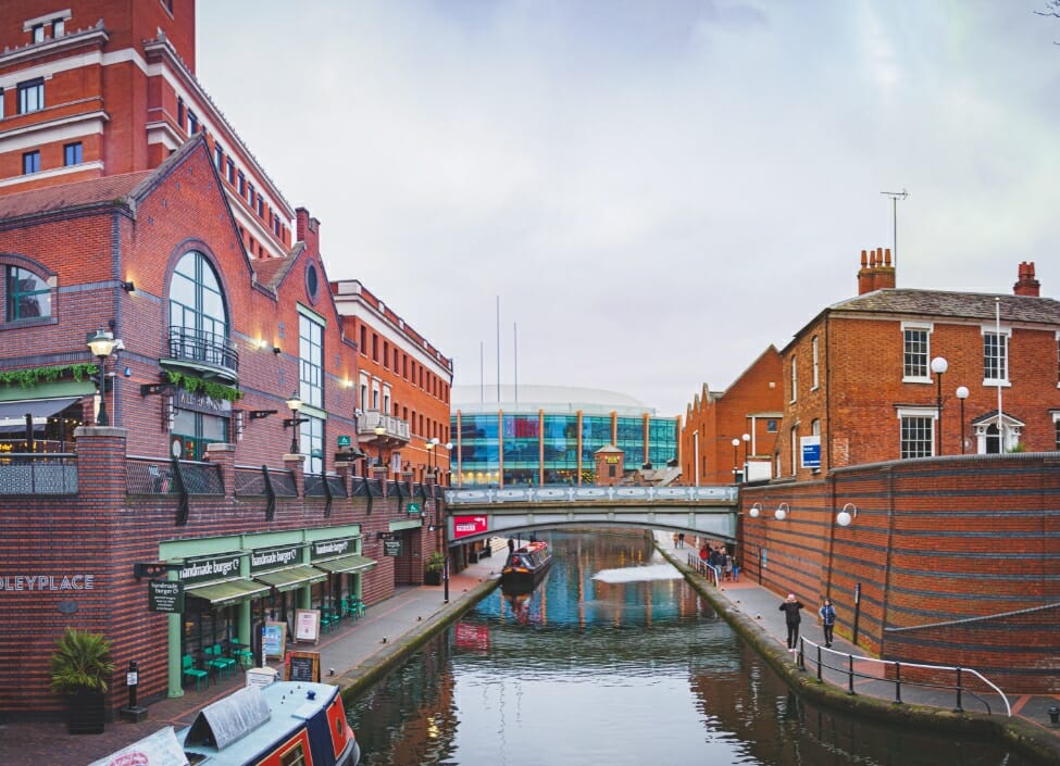 Birmingham Canal at Brindley Place with red brick buildings on either side, canal boats, and people walking on the footpaths.