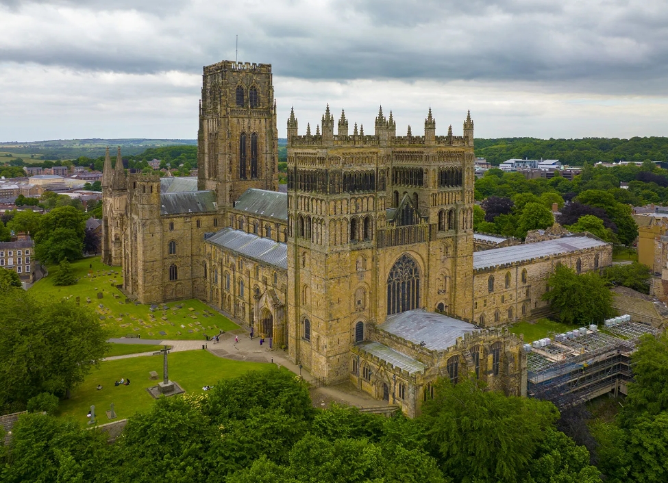 An aerial view of Durham Cathedral, a tall sandstone building surrounded by grass and trees.
