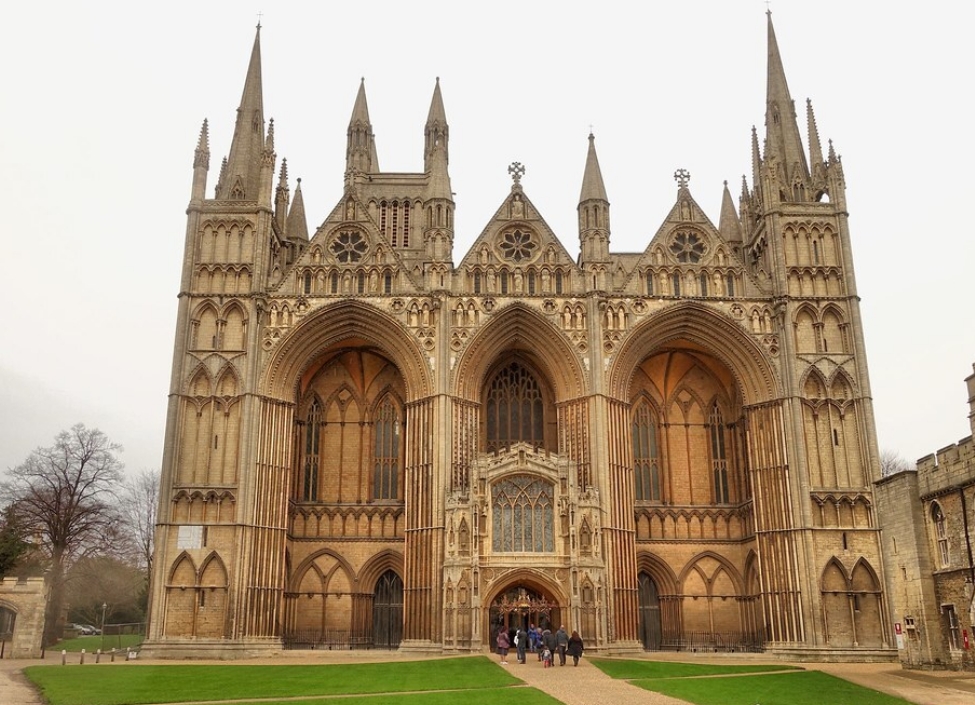 Peterborough Cathedral a tall gothic building made from limestone with grass and people in front