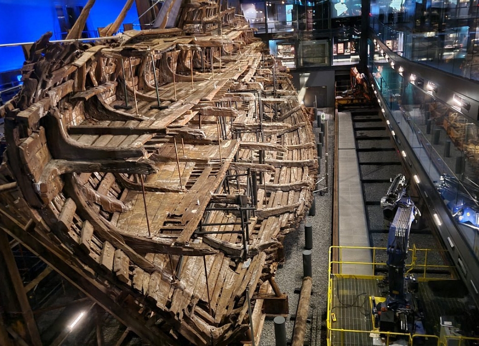 Wreckage of the Mary Rose boat in the Mary Rose Museum in Portsmouth with lighting and a viewing gallery behind glass.