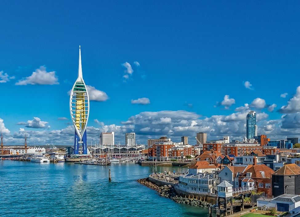 The tall Spinnaker Tower in Portsmouthsurrounded by sea and red brick buildings.