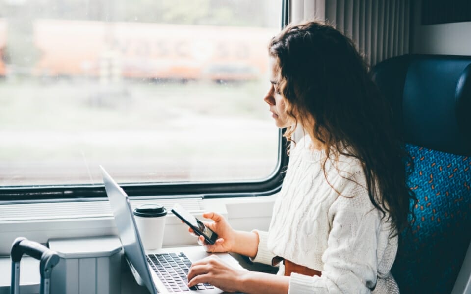 passenger on train booking train tickets on their phone while working on laptop