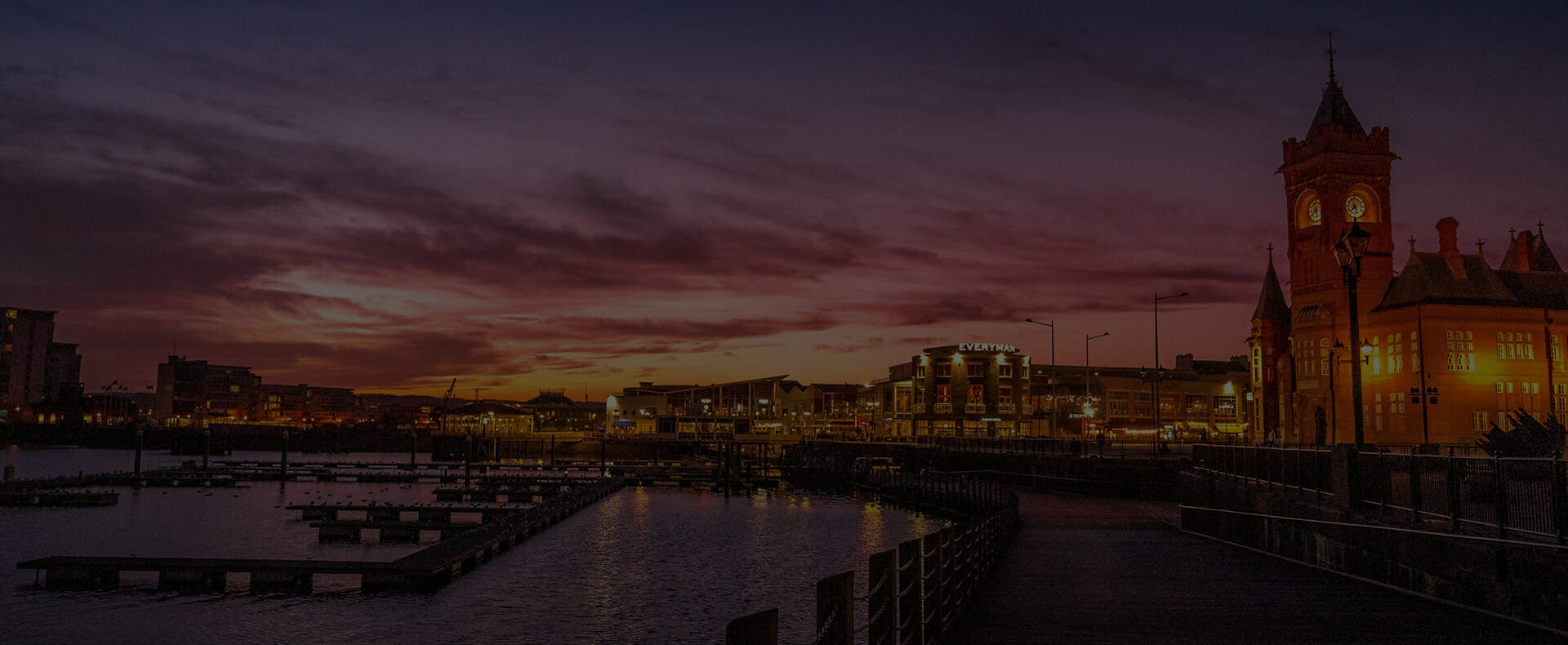 cardiff city bay at night with building lit up by the river taff with a sunset sky