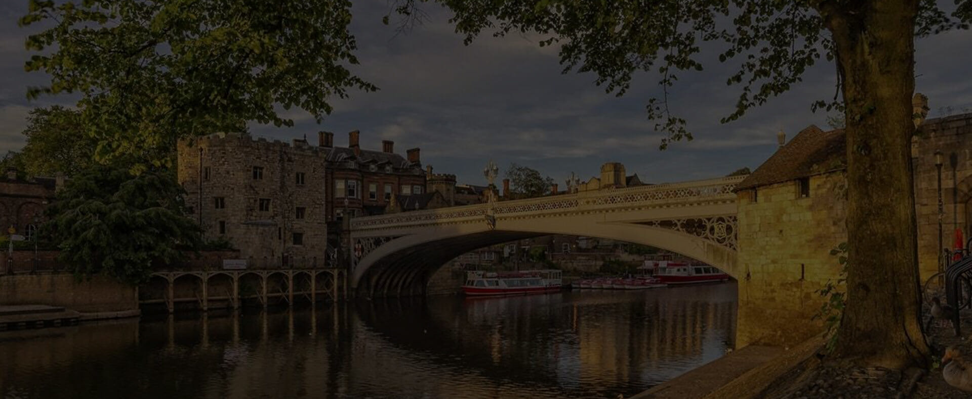 york city lendale bridge over river ouse during the day with boats on the river and trees and buildings to the side