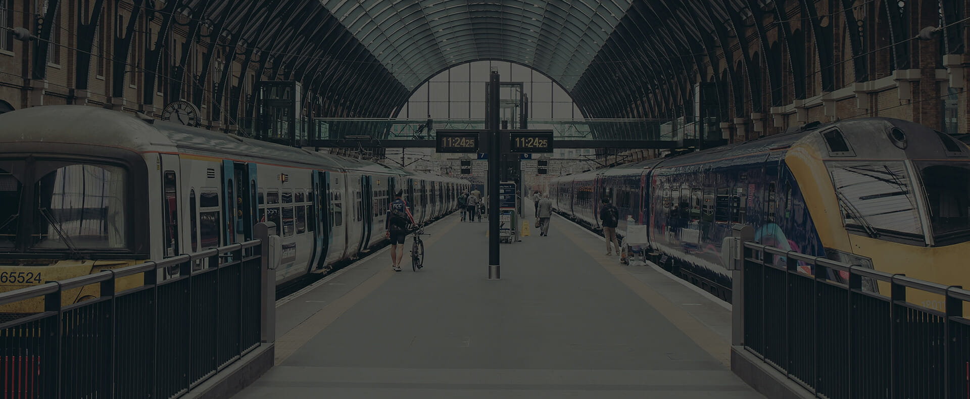 two trains waiting at platform at london kings cross station with pedestrians and a cyclist walking