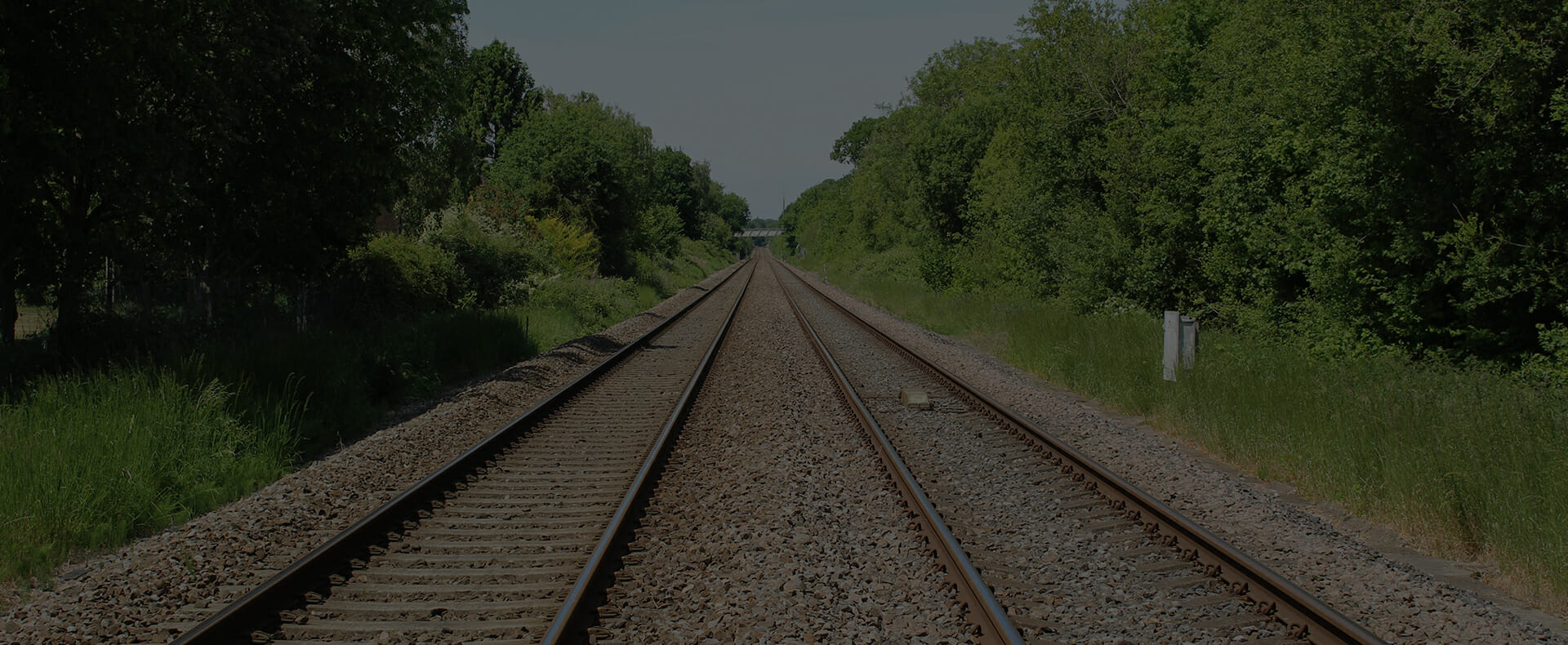 trainline rails in countryside with trees and grass either side and bridge in distance