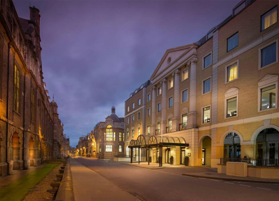 Hilton Cambridge City Centre hotel situated on a quiet street, at night with buildings on either side and a cloudy sky