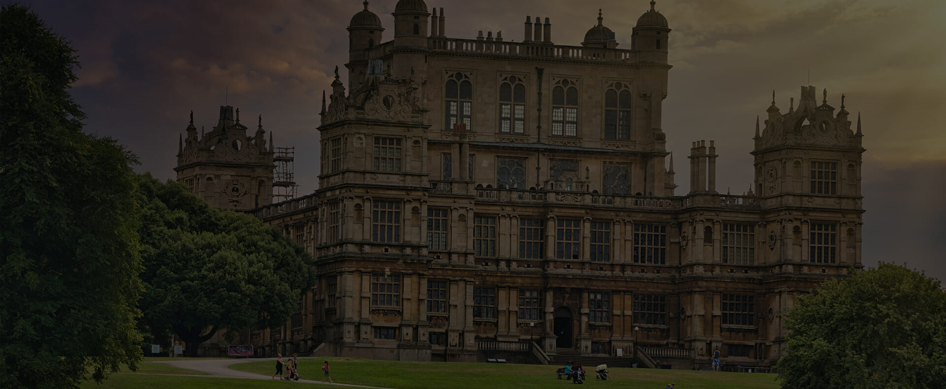 a grand and old building, wollaton hall in nottingham surrounded by grounds and trees with people walking
