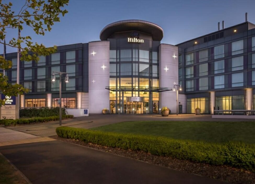 grey Hilton Reading hotel with four storeys and lights on the ground floor behind a grassy area