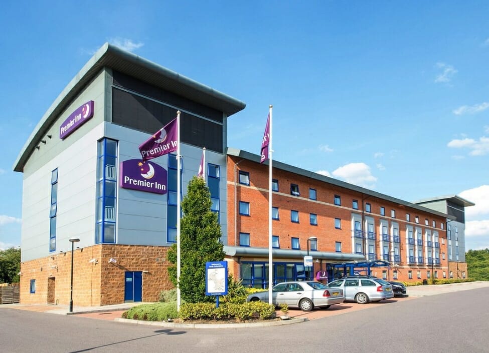 Premier Inn Banbury M40 hotel with a car park and cars outside and flags with the Premier Inn logo