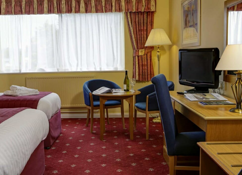 Best Western Tiverton Hotel room with twin beds, red carpet, a desk, table, and chairs
