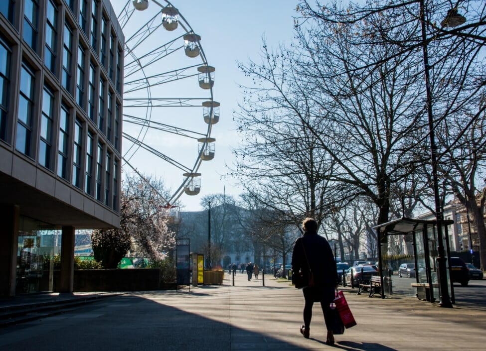 person walking on cheltenham promenade street with ferris wheel trees and building in background