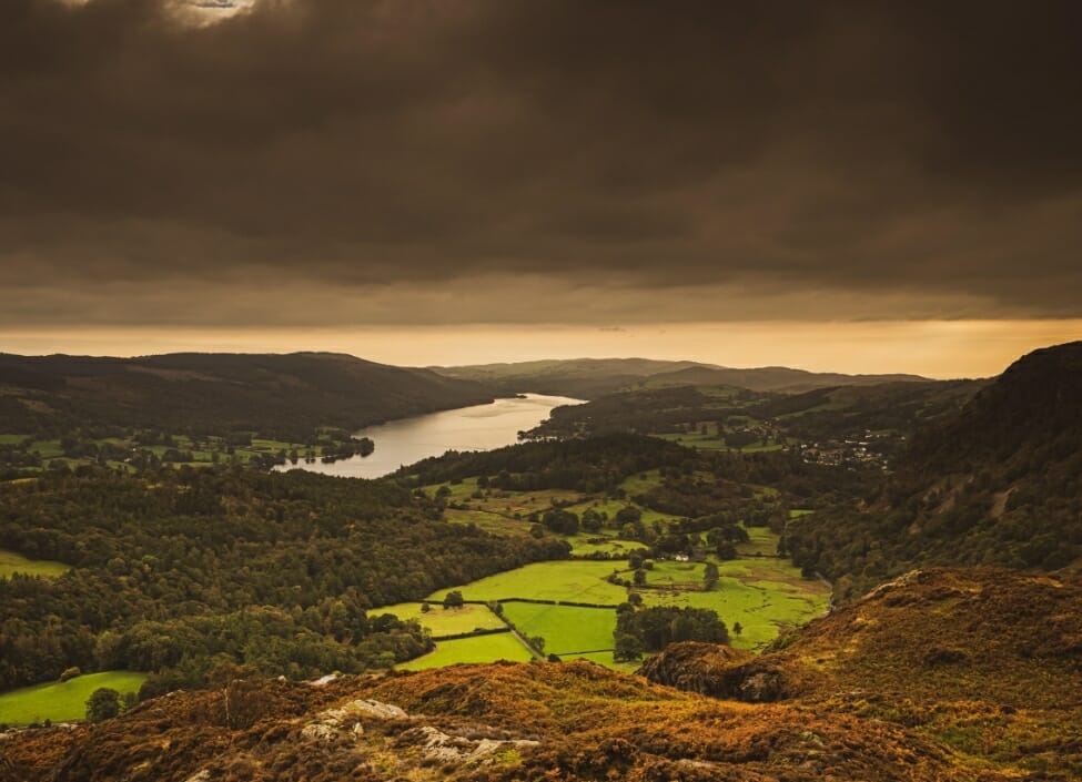 holme fell coniston with coniston water trees and fields and a dark cloudy sky
