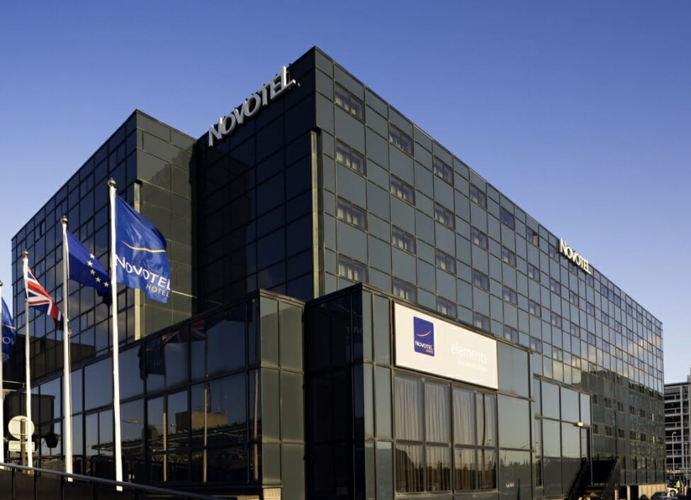 novotel birmingham airport hotel with numerous windows during the day with flagpoles outside