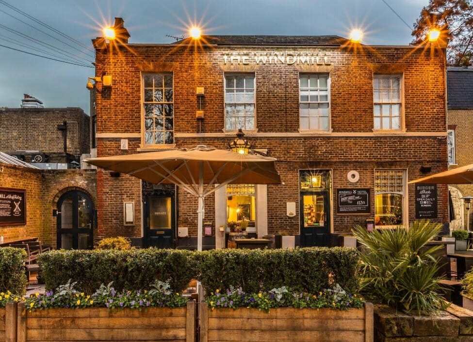 exterior of windmill hotel clapham at night, a bricked building with lighting a partially covered beer garden in front and planters
