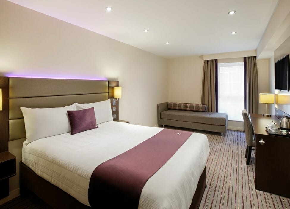 Premier Inn Romford Central hotel room lit with a bed, sofa, desk and side tables