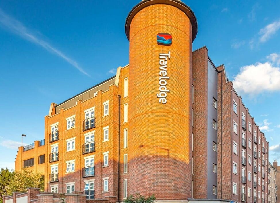 Travelodge London Romford Hotel, a bricked building with a blue sky behind and trees surrounding