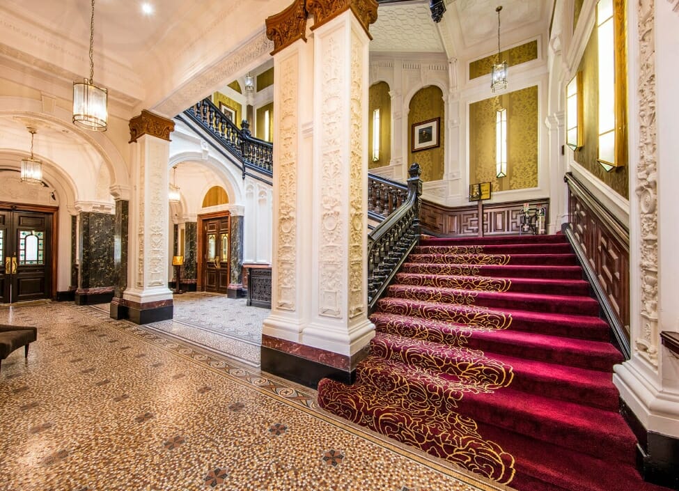 Inside the DoubleTree by Hilton Hotel and Spa Liverpool with a tiled floor and red carpeted stairs and white pillars