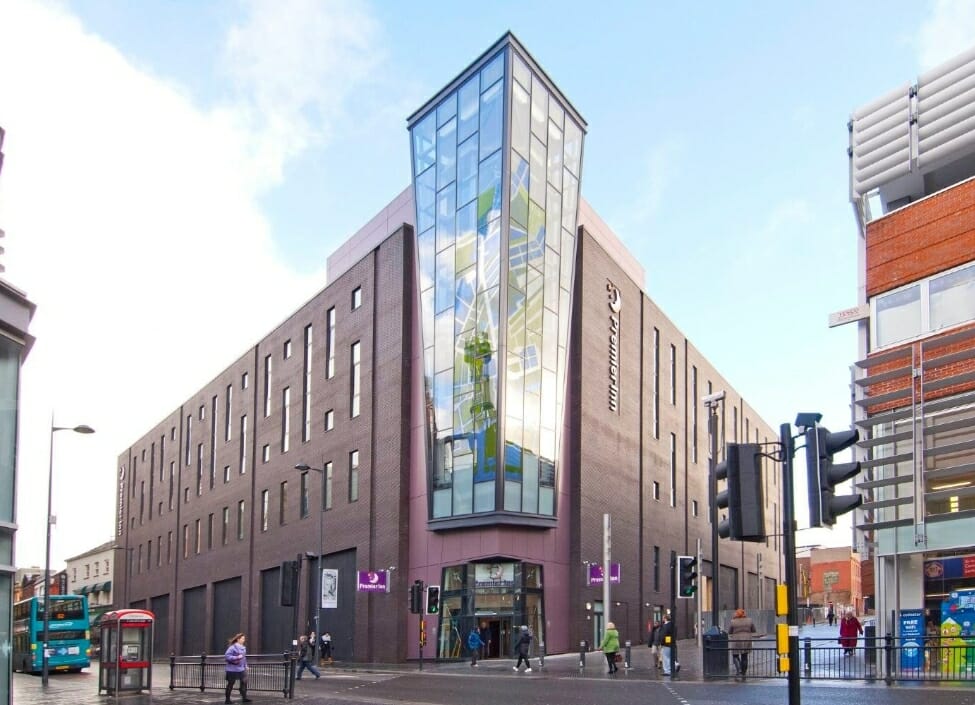 Premier Inn Liverpool City Centre Hotel, a bricked building with a glass front with pavements, traffic lights, pedestrians and a bus outside