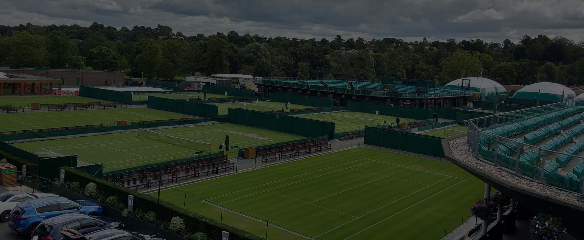 All England Lawn Tennis and Croquet Club, Wimbledon with eight gtass tennis courts and trees behind.
