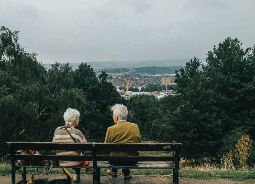 Two people sitting on a bench in Bristol with a dog and an aerial view of Bristol with trees in front