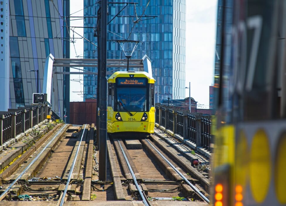 A yellow tram crossing a bridge in Manchester City with a tall building in the background