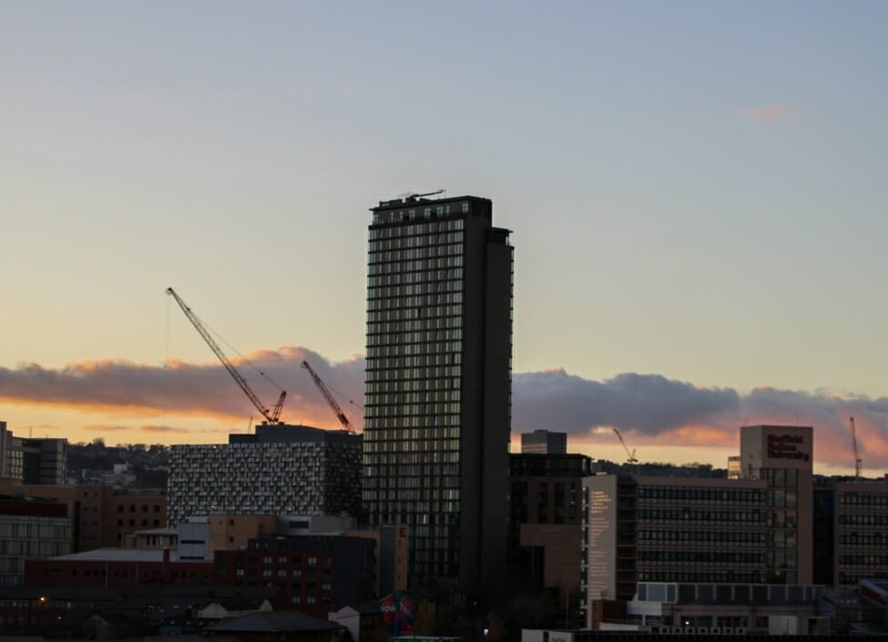 A view of the Sheffield City skyline at night with several buildings, cranes and a cloudy sky
