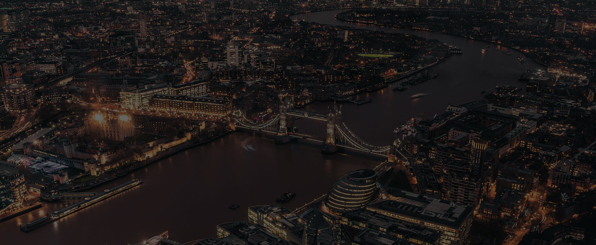 Aerial view of the river thames and tower bridge at night with buildings across London lit up.