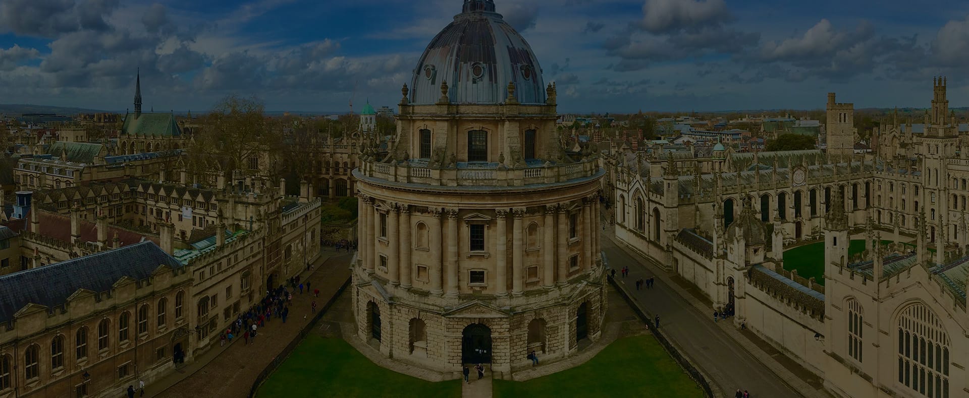 Radcliffe Camera at Oxford University, a tall domed building surrounded by smaller limestone buildings and grass.
