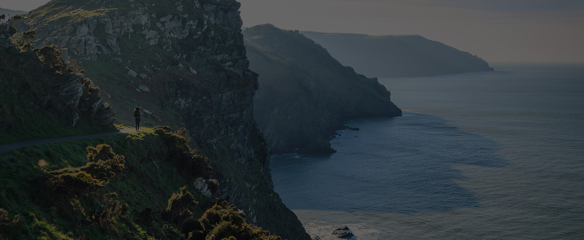 The jurassic coast with grassy cliffs next to the sea and a person walking on the path