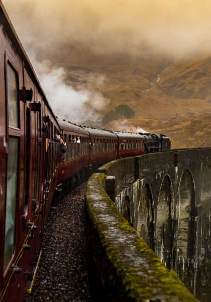 A steam train passing over Glenfinnan Viaduct in the Scottish Highlands with steam and landscape in the background.