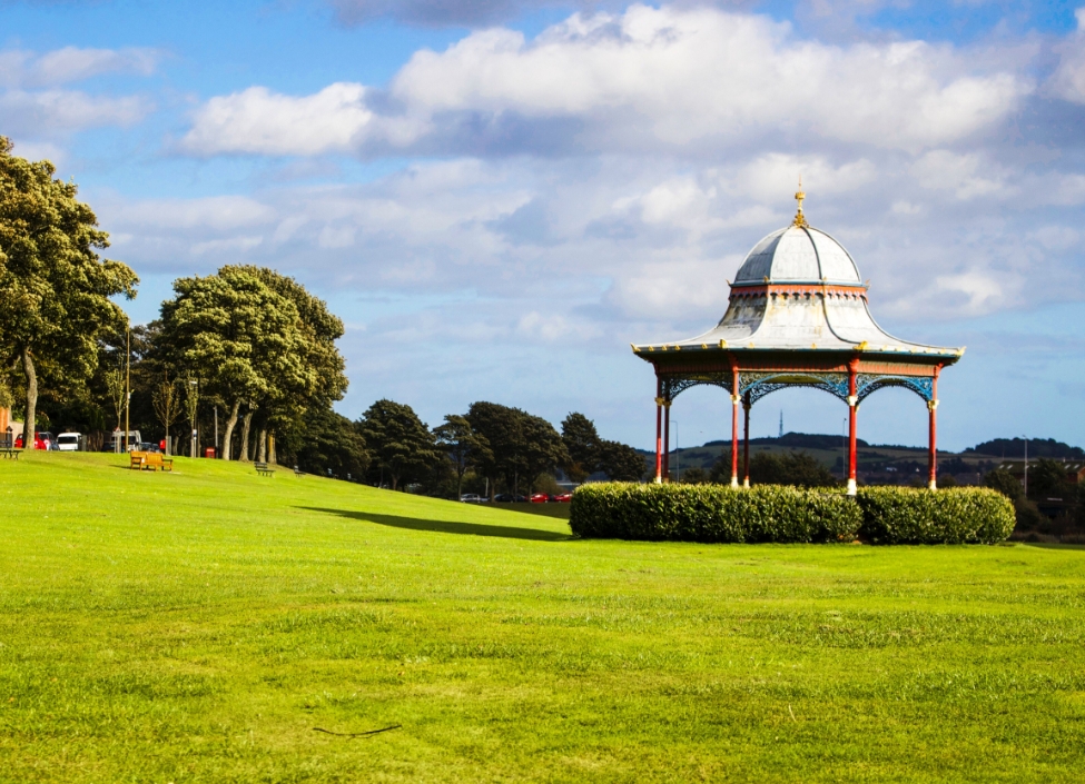 Magdalen Green Park in Dundee, a pavilion with grass and trees surrounding it and a bright and cloudy sky behind