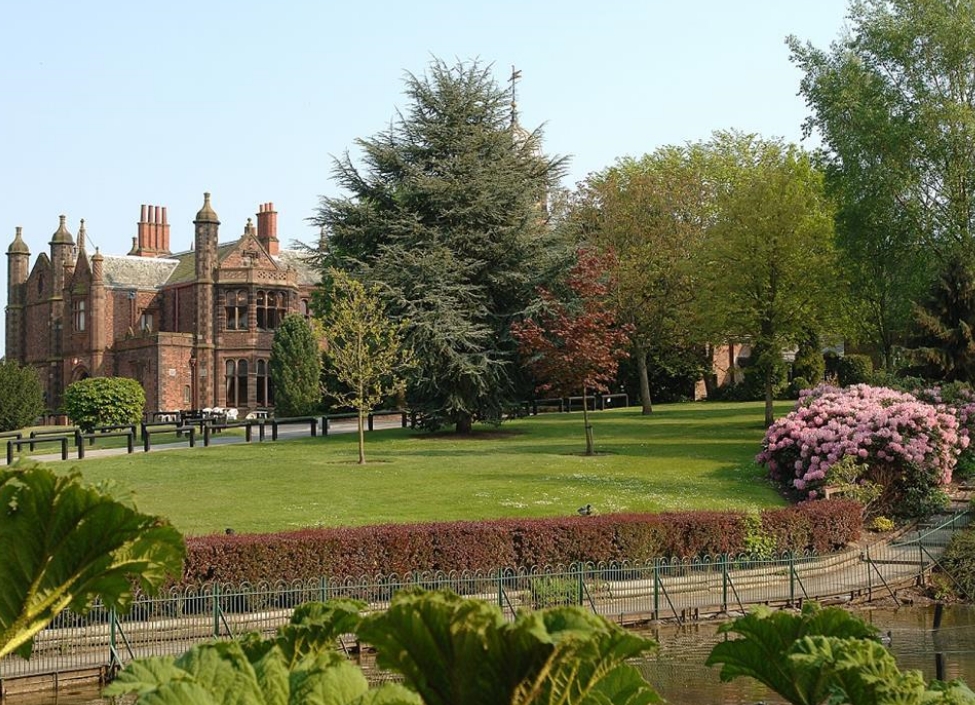 Walton Hall Gardens in Warrington, a tall red bricked building with grasses, trees, a hedge, and a path in front
