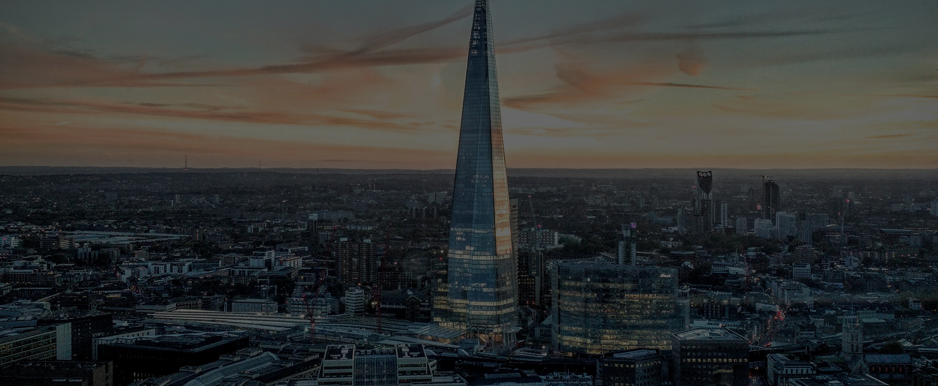 An aerial view of the shard lit up at night, surrounded by smaller buildings in London.