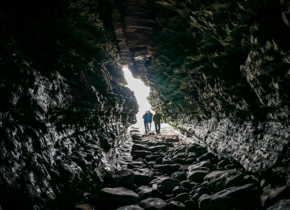 A tunnel by Southerndown Beach in Bridgend with large stones and people walking towards the light