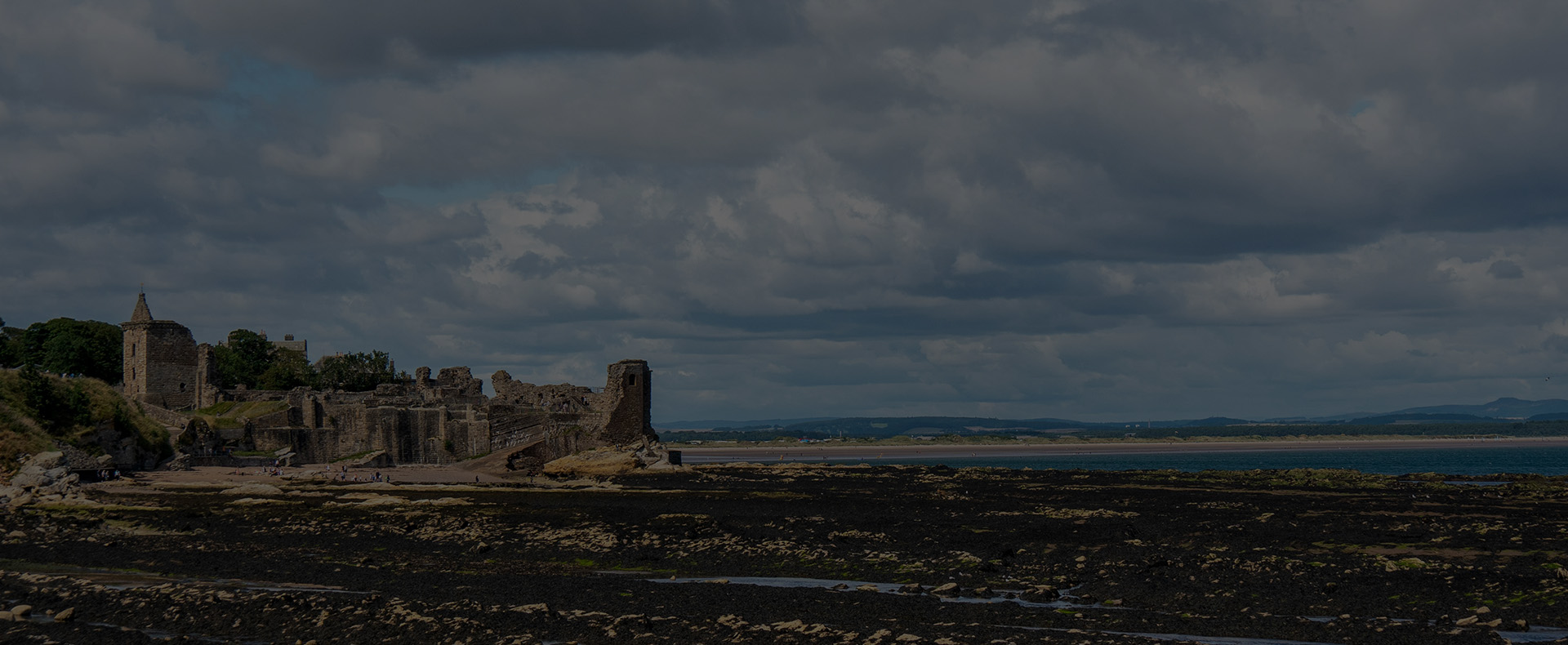 The ruins of St Andrews Castle in Scotland by the coast with rocks in front and a sandy beach behind.
