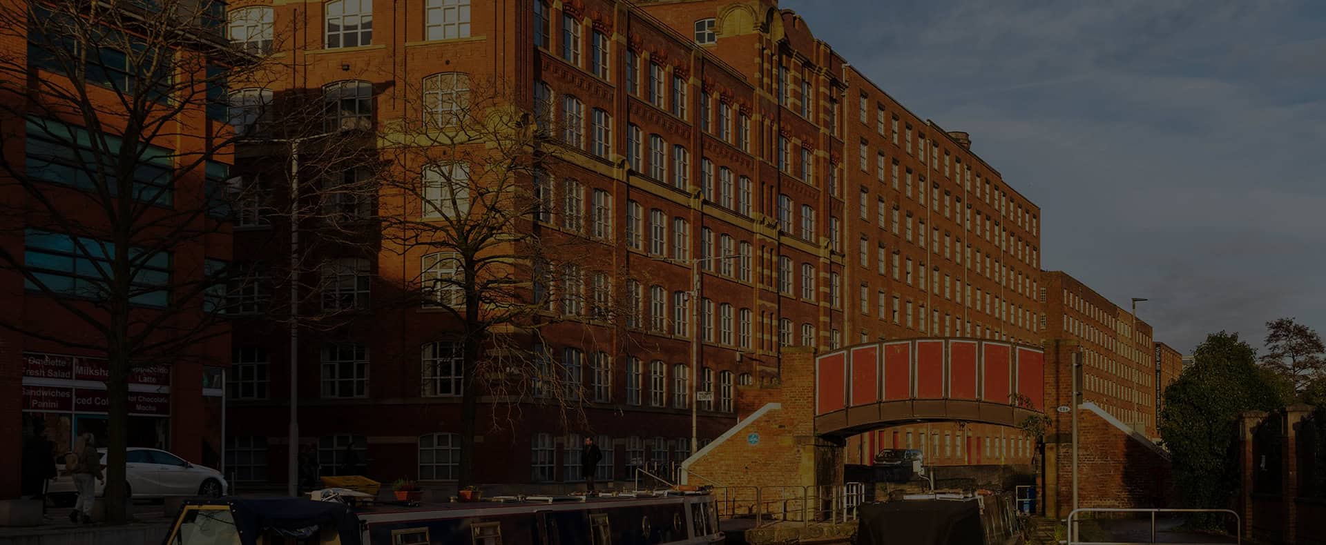 The Manchester Canl with a big red bricked building in the background and a red bridge crossing the canal.