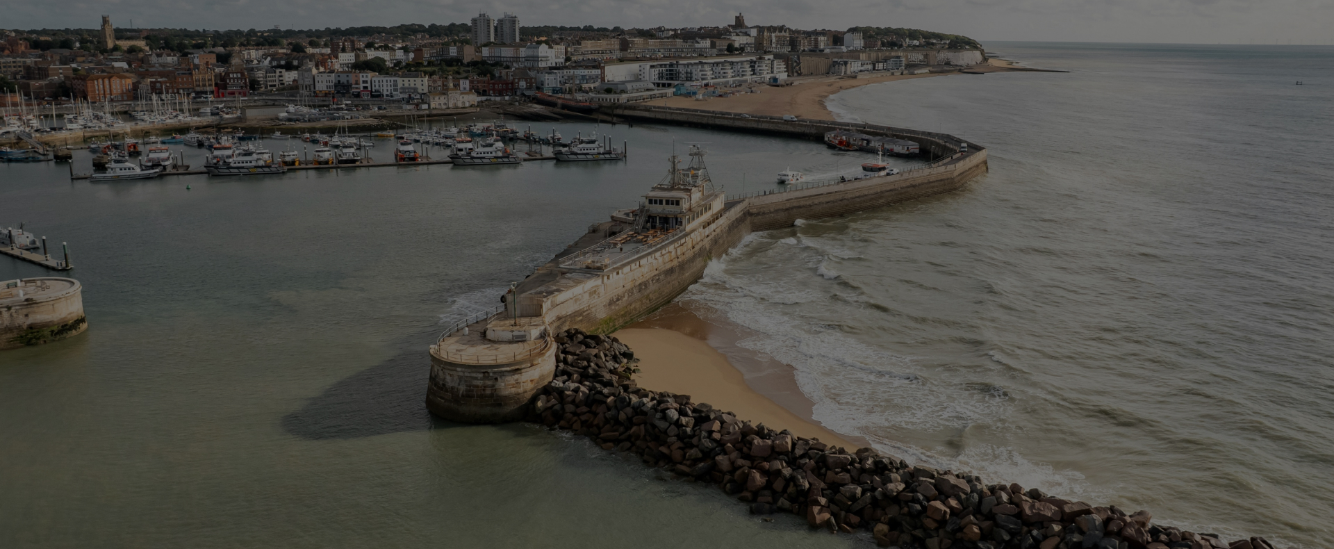 The harbour in Ramsgate with a pier, boats in the sea, and buildings in the background.