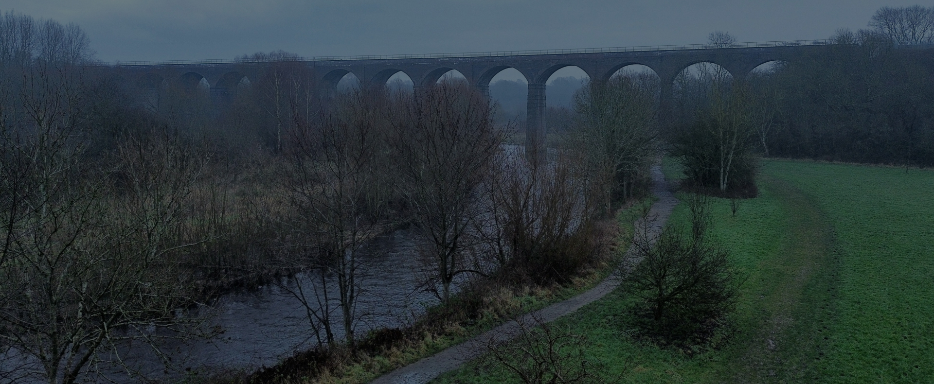 A viaduct bridge in Stockport over a river with trees and grass surrounding.