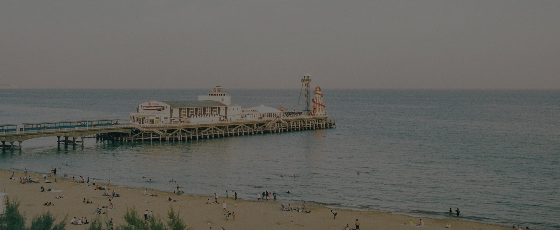 The pier in Bournemouth with buildings and a helter skelter on it next to the beach and sea.