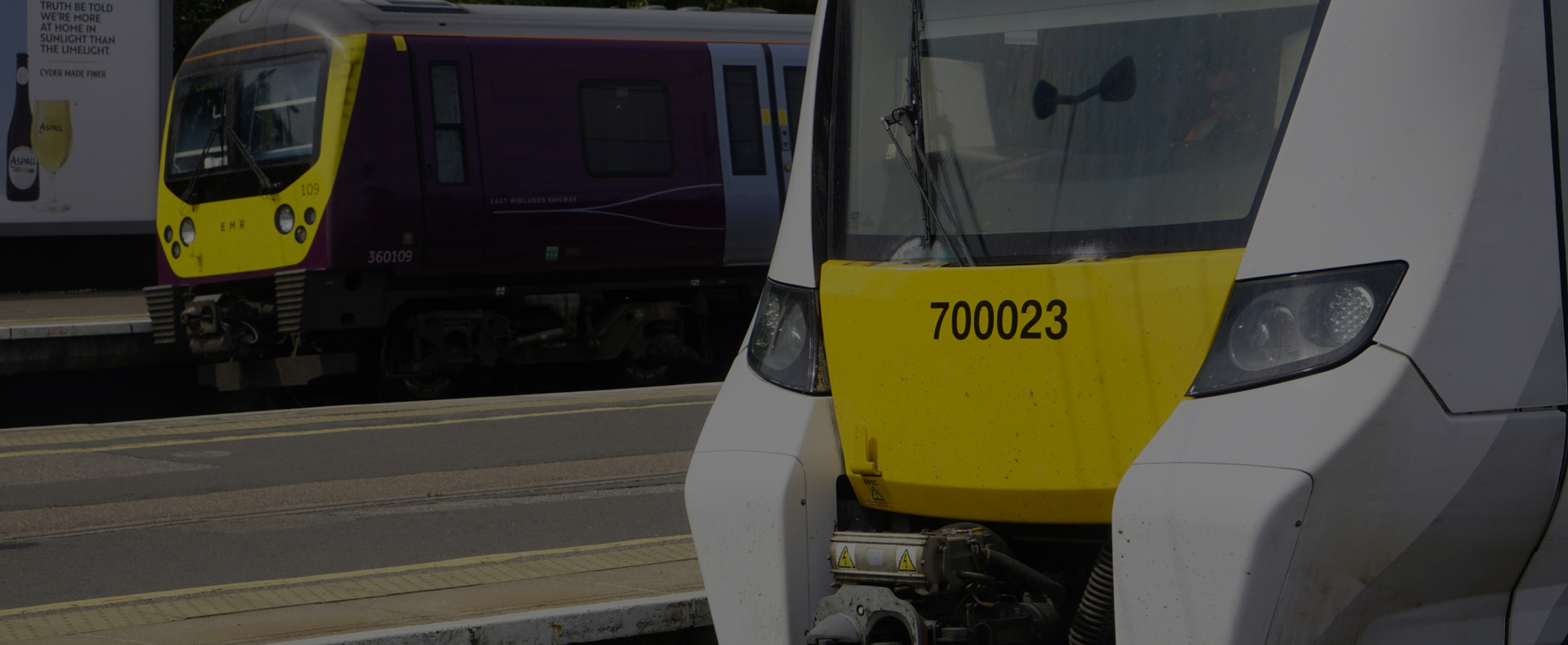 Two East Midlands Railway trains stationary on train platforms with an advertising billboard in the background.